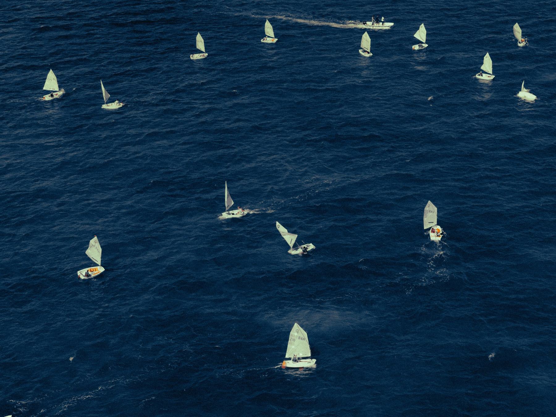 A fleet of racing sailboats on deep blue water, photographed from above